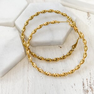 May include: A pair of gold-toned hoop earrings featuring a continuous twisted rope texture. The circular earrings are constructed from a polished metal wire that forms a spiral pattern throughout the entire circumference of each hoop.