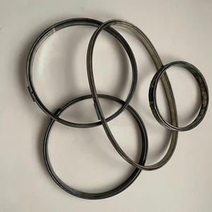 May include: Three circular metal hose clamps of varying sizes, each featuring a silver-toned finish and a threaded screw mechanism for tightening. The clamps are arranged in an overlapping configuration, showcasing their metallic texture and circular form.
