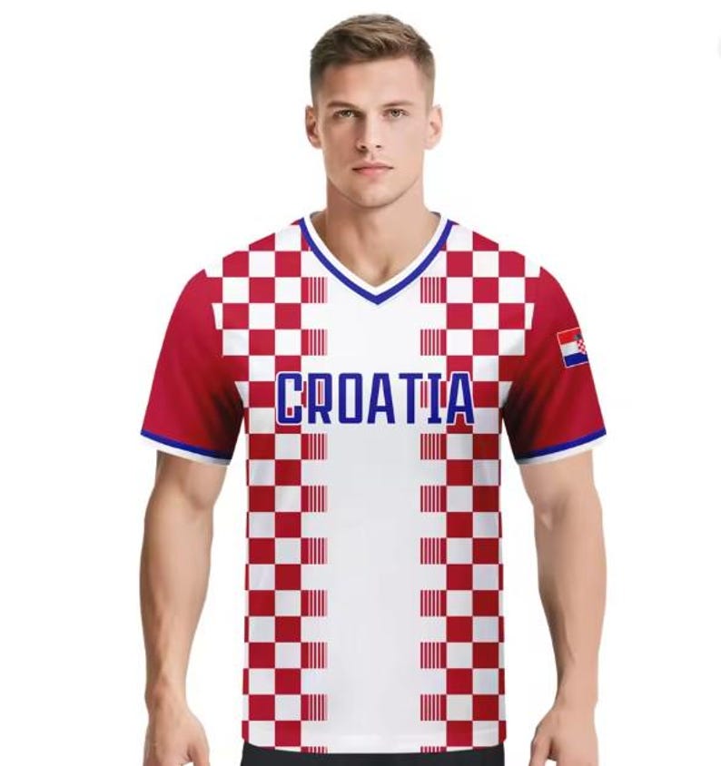 May include: A Croatia football shirt in white and red check pattern, with the word "CROATIA" in blue across the chest. The shirt features a V-neck and a small Croatian flag on the sleeve.