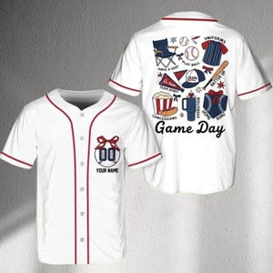 May include: White baseball jersey with red trim and buttons. The front features a bow design with the number "00" and the text "YOUR NAME". The back displays baseball-themed graphics and the words "Game Day".