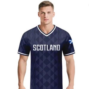 May include: A dark blue V-neck t-shirt featuring a repeating geometric diamond pattern and vertical wavy lines. The word SCOTLAND is printed in white capital letters across the chest, and a small Scottish flag emblem is visible on the left sleeve.