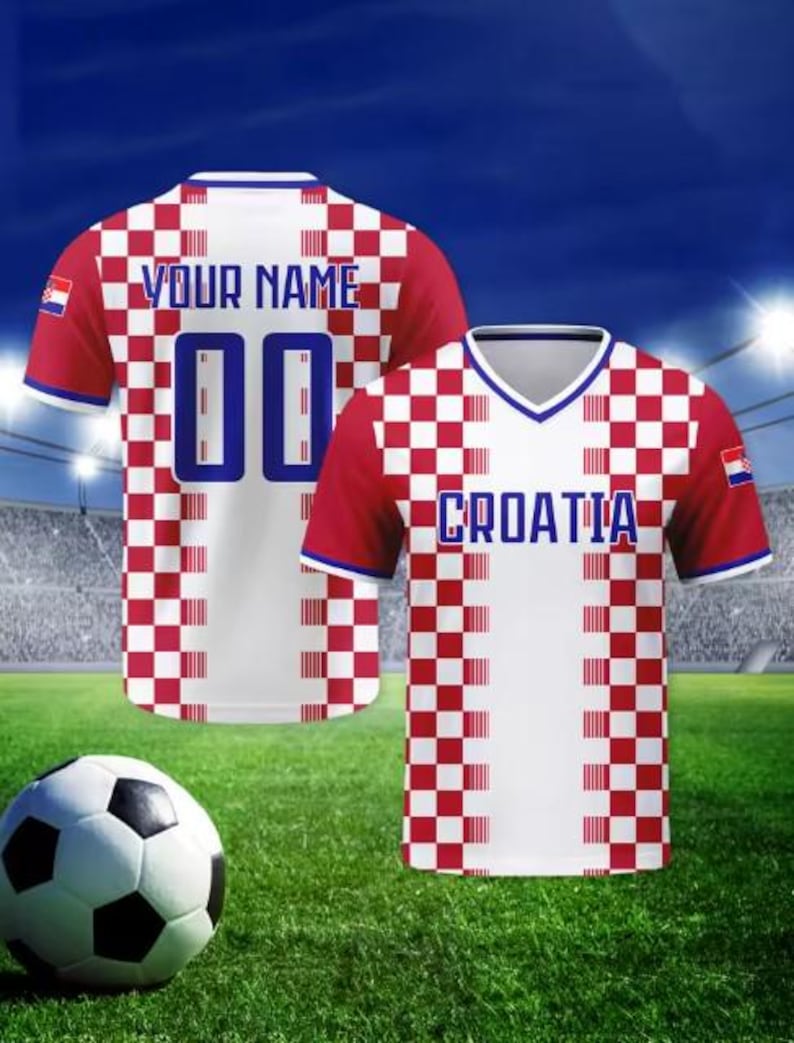 May include: Two Croatia football shirts with red and white chequered patterns, the text "YOUR NAME" and the number "00" on the back. The other shirt has "CROATIA" printed on the front. A football rests on the green grass.