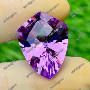 Könnte beinhalten: Ein schildförmiger facettierter Edelstein mit einem leuchtend violetten Farbton und komplexen geometrischen Schliffen, die lichtreflektierende Muster erzeugen. Der Stein trägt das wiederholte Wasserzeichen Mehakgems auf der Oberfläche.