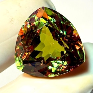 May include: A faceted, triangular gemstone with a vibrant display of colors. The gem features a mix of green, orange, and red hues, with a central area of lighter green. The cut of the stone creates multiple facets, enhancing its brilliance.
