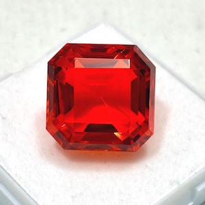 May include: A faceted, rectangular-cut, vibrant red gemstone. The gem has a symmetrical, octagonal shape with a polished surface, reflecting light. The gemstone is likely a ruby or a similar precious stone, suitable for jewelry.