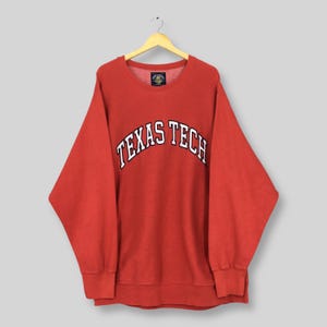 Può includere: Una felpa rossa Texas Tech con scritte bianche arcuate. La felpa girocollo ha maniche lunghe e orlo e polsini a coste. La felpa è appesa a una gruccia di legno.