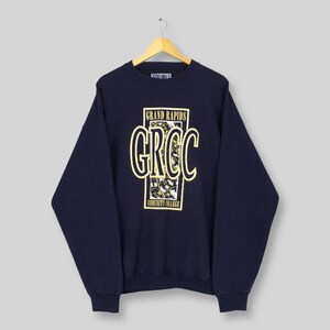 May include: Navy blue sweatshirt with the text "GRAND RAPIDS GRCC COMMUNITY COLLEGE" in yellow and white. The sweatshirt is hanging on a wooden hanger.