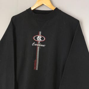 May include: Black sweatshirt with the word "Carolina" in script and a logo with the letters "NC" inside an oval. Vertical stripes in red and white are on the front, with the words "Tar Heels" vertically.