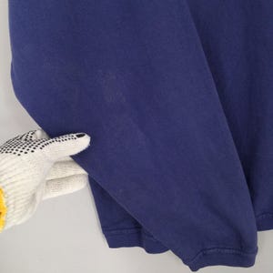May include: A close-up of a navy blue long-sleeved top. The top is made of a soft material and has a ribbed cuff. The sleeve is being held by a gloved hand.