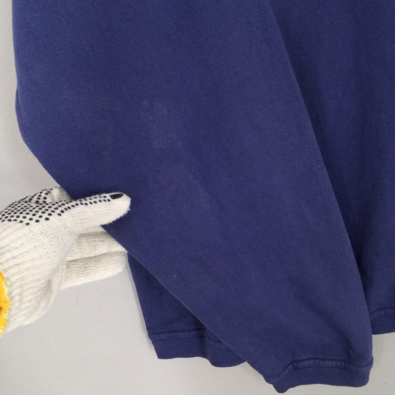 May include: A close-up of a navy blue long-sleeved top. The top is made of a soft material and has a ribbed cuff. The sleeve is being held by a gloved hand.