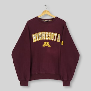 May include: Maroon sweatshirt with "MINNESOTA" in gold lettering and a gold "M" logo. The sweatshirt is hanging on a wooden hanger. The sweatshirt has a crew neck and long sleeves. The sweatshirt is a vintage item.