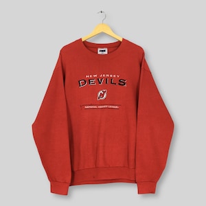 May include: A red sweatshirt with the text "NEW JERSEY DEVILS" in white and black lettering. The sweatshirt also features the team's logo and the text "NATIONAL HOCKEY LEAGUE."