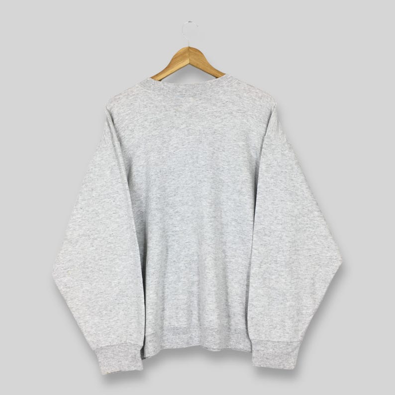 May include: A grey sweatshirt hangs on a wooden hanger. The crew neck sweatshirt has long sleeves and ribbed cuffs and hem. The garment is made of a soft, comfortable material.