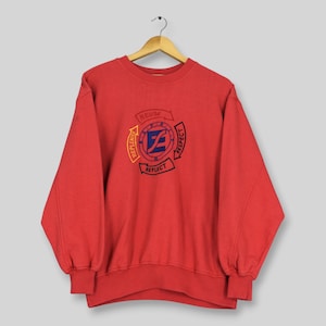 Può includere: Una felpa rossa a maniche lunghe con girocollo caratterizzata da una grafica circolare centrale con un logo blu a forma di lettera E. Il design include frecce disposte in cerchio con le parole REUSE, RESPECT, REFLECT e REPLENISH in nero e giallo.