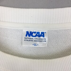 May include: A white crew neck sweatshirt featuring a white fabric tag on the inside collar. The tag displays the blue NCAA logo, the text National Collegiate Athletic Association, and the size LL printed in blue on a white background.