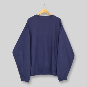 May include: A navy blue sweatshirt suspended from a wooden hanger. The garment features a crew neck and long sleeves. The material looks soft and comfortable. The sweatshirt is a solid colour, without any visible graphics or patterns.