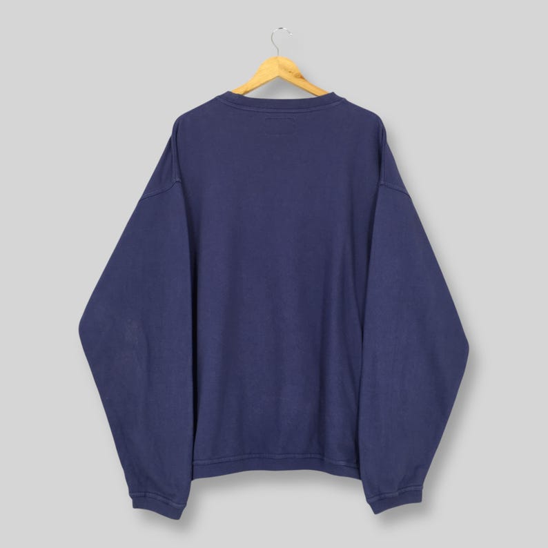 May include: A navy blue sweatshirt suspended from a wooden hanger. The garment features a crew neck and long sleeves. The material looks soft and comfortable. The sweatshirt is a solid colour, without any visible graphics or patterns.