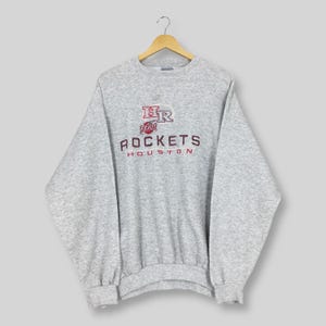 Puede incluir: Una sudadera gris jaspeada con el texto "Rockets Houston" en granate y blanco. La sudadera tiene cuello redondo y mangas largas. El logotipo presenta "HR" encima de la palabra "Rockets".