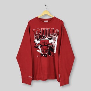 May include: Red Bulls sweatshirt with the team logo and text "Bulls Chicago Basketball". The sweatshirt is hanging on a wooden hanger. The Mitchell & Ness logo is visible on the sleeve.