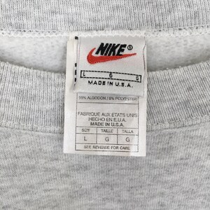 May include: Close-up of a grey sweatshirt with a Nike label. The label shows the Nike logo, text reading "MADE IN U.S.A.", and size details. The fabric composition is 95% cotton and 5% polyester.