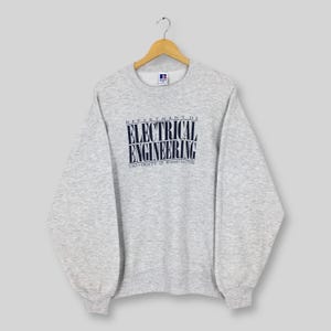 May include: A light gray Russell sweatshirt with the text "DEPARTMENT OF ELECTRICAL ENGINEERING UNIVERSITY OF WASHINGTON" in navy blue. The sweatshirt is hanging on a wooden hanger.