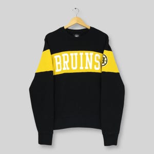 May include: Black sweatshirt with yellow stripes on the sleeves and a yellow band across the chest. The word "BRUINS" is printed in white block letters across the chest. A logo is on the right sleeve and the brand logo is at the top.
