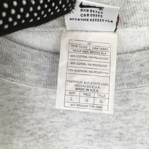 May include: Close-up of a grey sweatshirt label with the Nike logo. The label includes text with the RN, CA, and RFC numbers, along with the fabric composition: 95% cotton and 5% polyester. The label also states "Made in U.S.A."