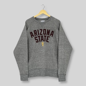 Puede incluir: Una sudadera gris de la Universidad Estatal de Arizona con las palabras "ARIZONA STATE" en letras de bloque granates. Un logotipo de tridente dorado está debajo de la palabra "STATE". La sudadera está colgada en una percha de madera.