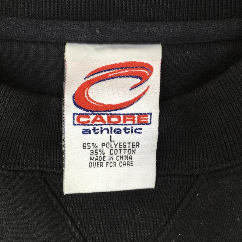 May include: Close-up of a black sweatshirt tag. The tag features the "CADRE athletic" logo in red and white. The tag also includes the fabric composition: 65% polyester, 35% cotton. The tag also states "MADE IN CHINA".