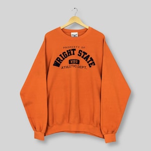 May include: An orange sweatshirt featuring the text "PROPERTY OF WRIGHT STATE ATHLETIC DEPT." in black. The sweatshirt has long sleeves and a crew neck. The fabric appears to be a soft, comfortable material.