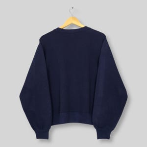 May include: Navy blue sweatshirt hanging on a wooden hanger. The sweatshirt has a crew neck and ribbed cuffs and hem. The garment is made of a soft, comfortable material.