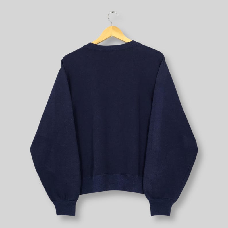 May include: Navy blue sweatshirt hanging on a wooden hanger. The sweatshirt has a crew neck and ribbed cuffs and hem. The garment is made of a soft, comfortable material.
