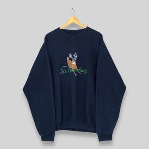 May include: Navy blue sweatshirt with a graphic of a deer with antlers and the text "Six Point Stag" in green. The sweatshirt is hanging on a wooden hanger against a light background.