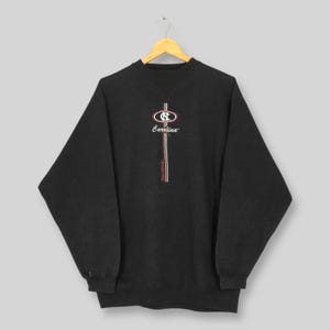 May include: Dark gray sweatshirt with the word "Carolina" in script and a logo featuring the letters "NC" in a circular design. The sweatshirt has a crew neck and long sleeves. The design includes red and white stripes.
