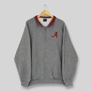 May include: A gray sweatshirt with a burgundy collar and the letter "A" embroidered on the chest. The sweatshirt has a quarter-zip closure and long sleeves. The garment is hanging on a wooden hanger.
