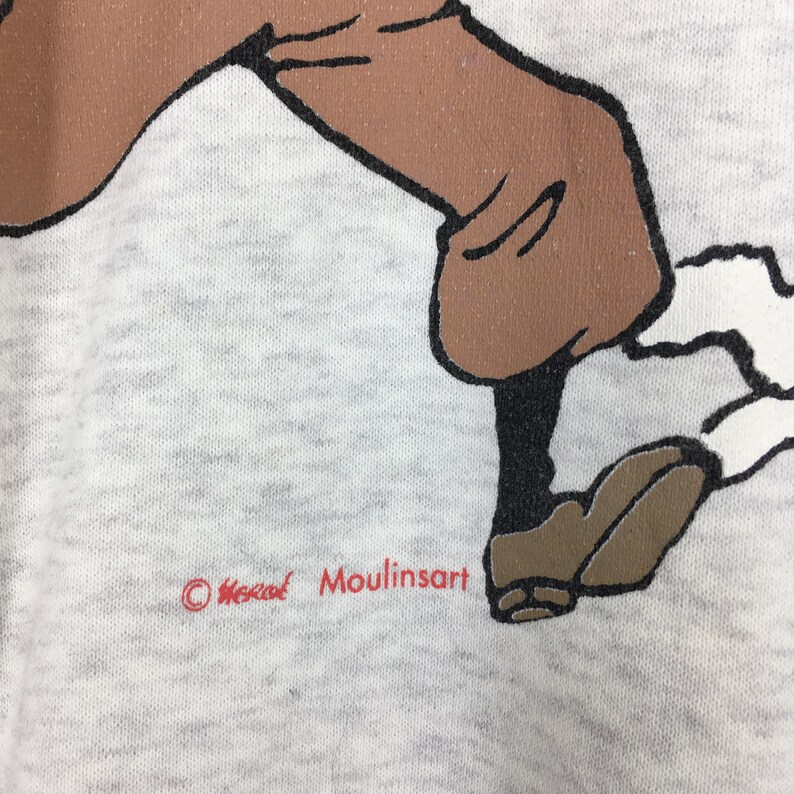 Peut inclure: Gros plan sur un tissu gris clair avec une illustration de dessin anim&eacute; des jambes et des pieds dans des chaussures marron. Le texte "&copy; Herg&eacute; Moulinsart" est imprim&eacute; en rouge en bas.
