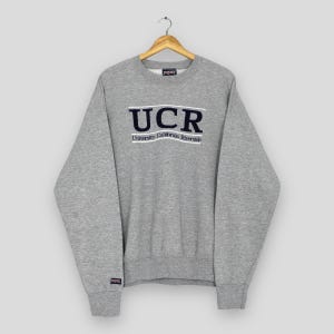 May include: A gray crew neck sweatshirt with the text "UCR" in white block letters above the words "University California Riverside" in a smaller font. The sweatshirt has long sleeves and a small logo on the left sleeve.