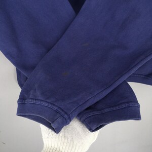 May include: Close-up of a navy blue sweatshirt sleeve. The sleeve is cuffed at the wrist and shows some discoloration. The fabric appears to be a soft, knit material. The image is well-lit, highlighting the texture and colour of the garment.
