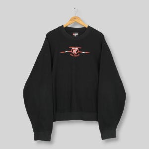 May include: Black crew neck sweatshirt featuring the text "Kingsdale Central Softball Red Devils" in red and white. The sweatshirt has long sleeves and a ribbed hem and cuffs. The sweatshirt is hanging on a wooden hanger.