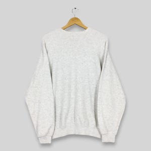 Peut inclure: Un sweat-shirt gris clair &agrave; manches longues, suspendu &agrave; un cintre en bois. Le sweat-shirt a un col rond et des poignets et un ourlet c&ocirc;tel&eacute;s. Le tissu semble &ecirc;tre une mati&egrave;re tricot&eacute;e douce.