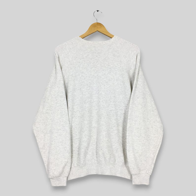Peut inclure: Un sweat-shirt gris clair &agrave; manches longues, suspendu &agrave; un cintre en bois. Le sweat-shirt a un col rond et des poignets et un ourlet c&ocirc;tel&eacute;s. Le tissu semble &ecirc;tre une mati&egrave;re tricot&eacute;e douce.