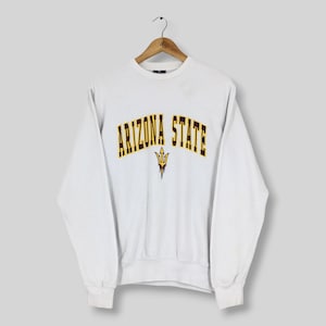 May include: A white long-sleeve crewneck sweatshirt featuring the text ARIZONA STATE in an arched maroon font with a yellow outline. Below the text is a yellow and maroon trident graphic. The garment has ribbed cuffs and a ribbed hem.