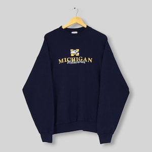 Peut inclure: Un sweat-shirt bleu marine à manches longues avec le texte MICHIGAN en lettres jaunes au-dessus du mot Wolverines en écriture blanche. Au-dessus du texte se trouve un carré jaune contenant un graphique blanc d'une silhouette de carcajou.