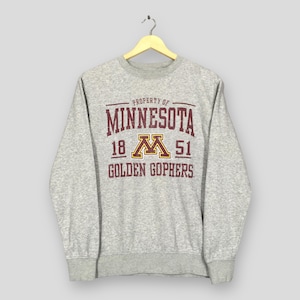 May include: A heather gray sweatshirt with the text "PROPERTY OF MINNESOTA 1851 GOLDEN GOPHERS" in maroon and gold. The sweatshirt is hanging on a wooden hanger.