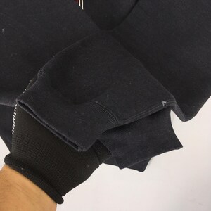 May include: Close-up of a black sweatshirt sleeve. The cuff is ribbed and black. The sleeve is folded over, revealing the inside of the sleeve. The fabric appears to be a soft, thick material.