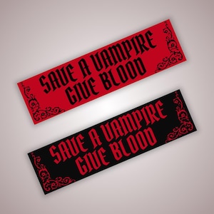 May include: Two rectangular stickers, one red and one black, with the phrase "SAVE A VAMPIRE GIVE BLOOD" in a gothic font. Each sticker has decorative corner flourishes in a contrasting color.
