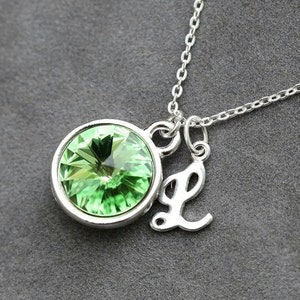 May include: A silver necklace with a green crystal pendant and a silver charm with the letter L.