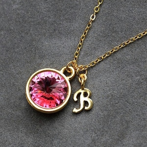 May include: A gold chain necklace with a pink crystal pendant and a gold charm with the letter "B".