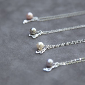 Puede incluir: Cuatro collares de plata con dijes de perlas. Cada collar tiene una perla de un color diferente: rosa, gris, blanco y gris. Las perlas están unidas a un dije de plata con una letra.