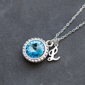 May include: A silver necklace with a blue crystal pendant and a silver charm with the letter L.